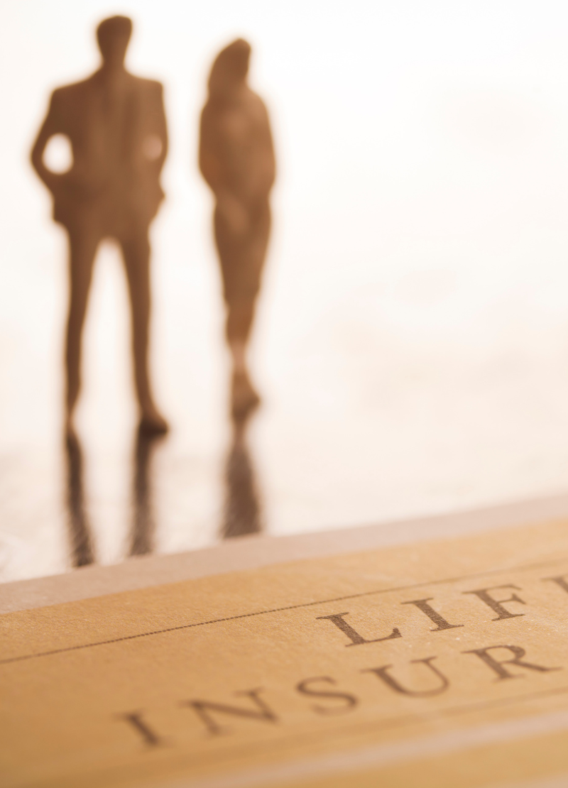 ife Insurance: Building Legacy Wealth and Becoming Your Own Bank A blurred image of two people standing behind a life insurance document, symbolizing the use of life insurance for legacy wealth building and the option to borrow against policies to become your own bank.
