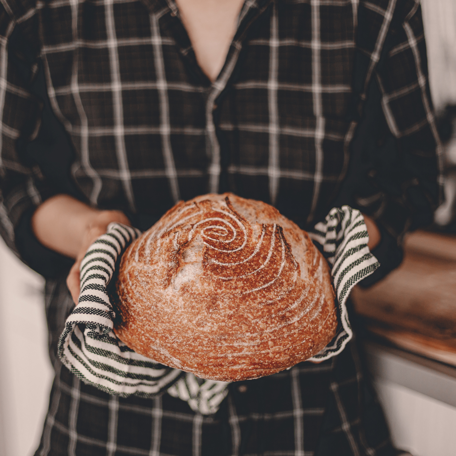 The Health Benefits of Baking Your Own Sourdough Person holding freshly baked sourdough bread loaf with a spiral design, symbolizing the art and health benefits of homemade bread.