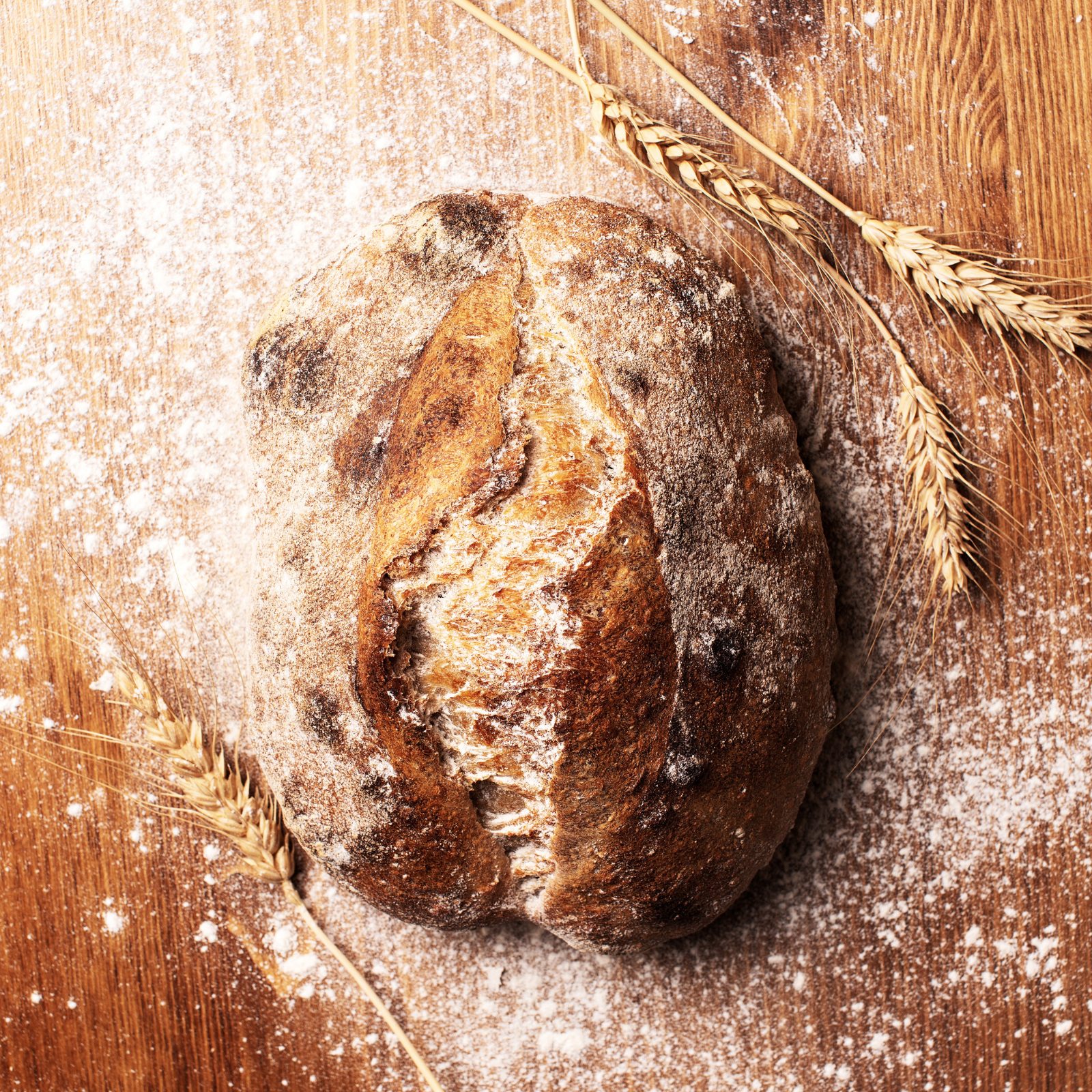 Mastering Sourdough Baking: Troubleshooting Made Easy "Golden crusted sourdough loaf on a floured wooden surface with wheat stalks, symbolizing artisan bread and baking perfection."