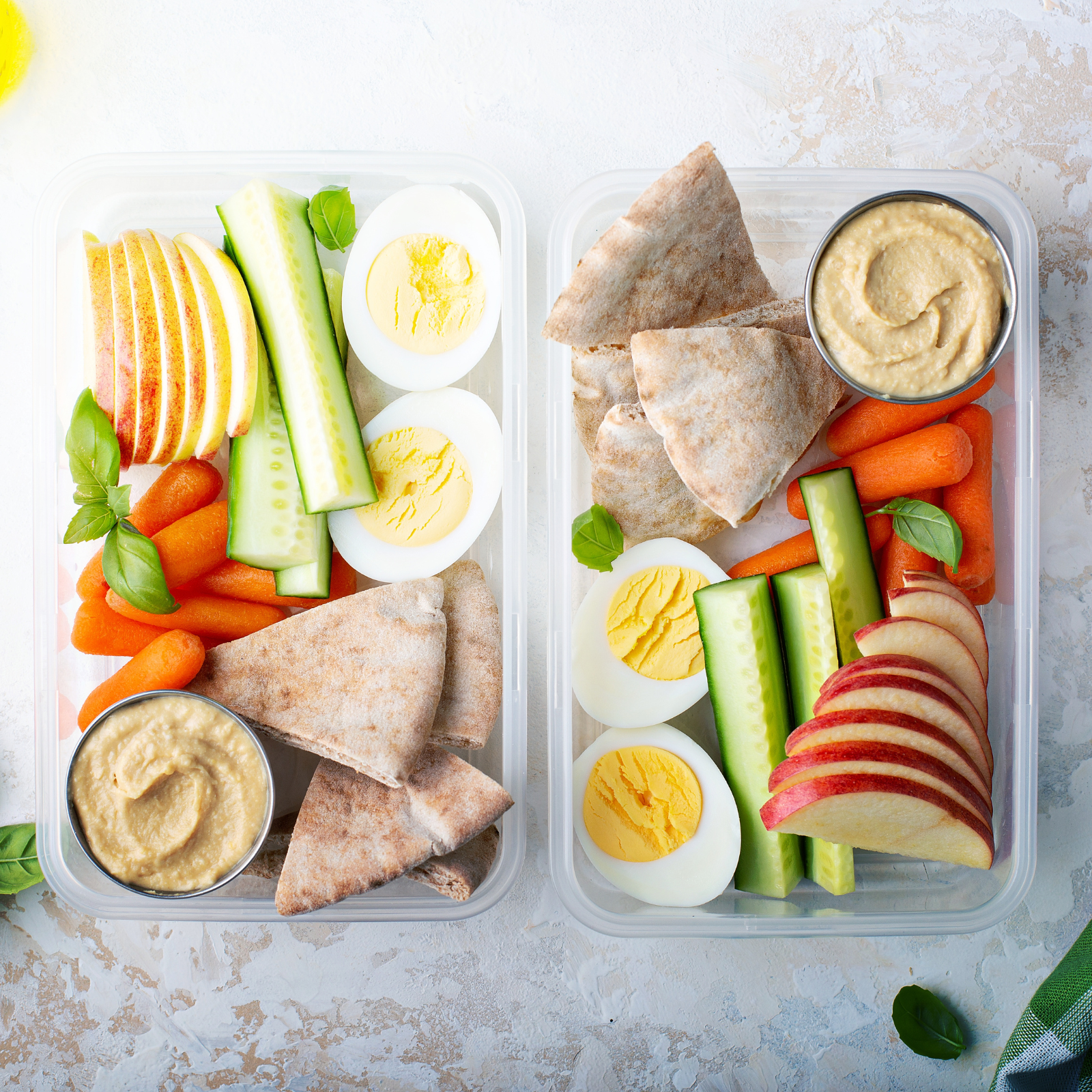 Balanced Snack Ideas for Busy Families | Wellness with Rachael Two clear lunch containers filled with hard-boiled eggs, cucumber, carrots, apple slices, pita bread, and hummus—balanced snack ideas from Rachael DeBoy of Wellness with Rachael in San Antonio, Texas.