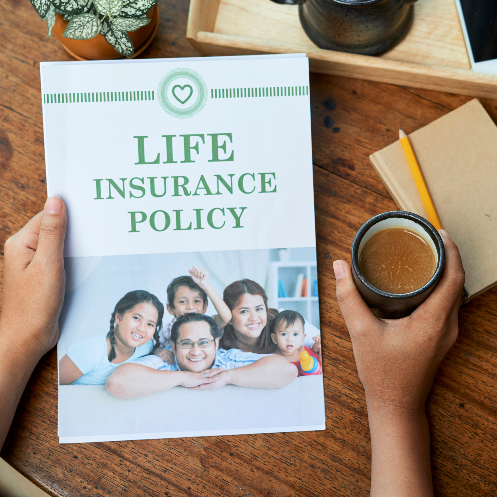 Why Life Insurance Matters for Every Stage of Life Hands holding a life insurance policy booklet with a smiling family on the cover, alongside a cup of coffee and notepad on a wooden table.