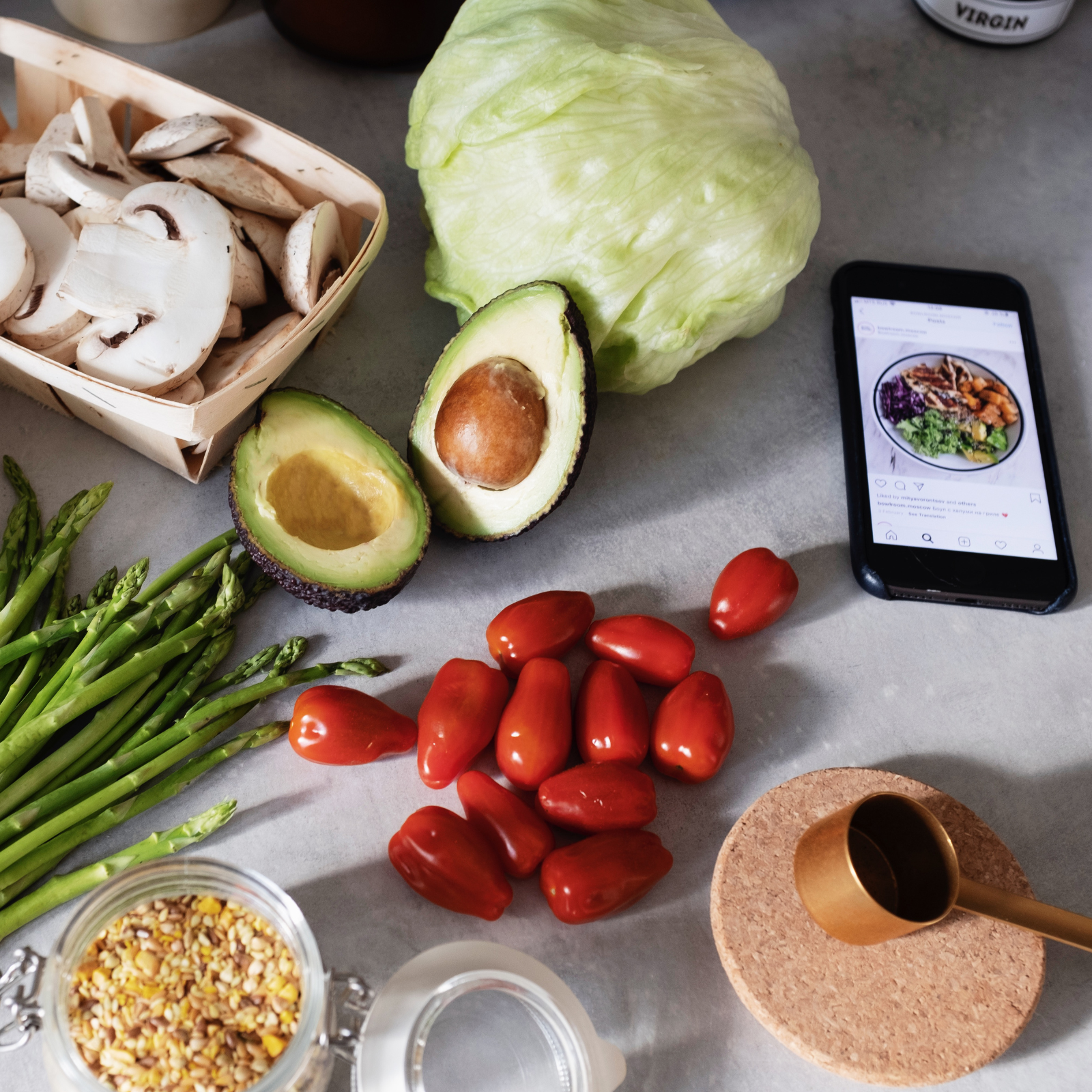 Whole Food Ingredients for Healthy Family Meals Flat lay of healthy whole foods including avocado, asparagus, tomatoes, mushrooms, lettuce, grains, and a smartphone displaying a meal inspiration photo.