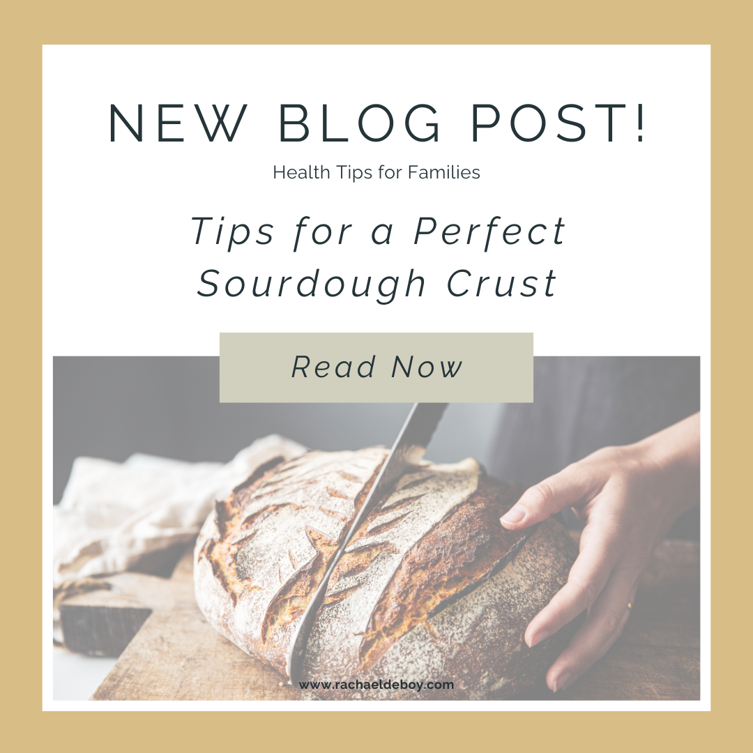 Hand slicing a crusty, golden-brown sourdough loaf on a wooden cutting board.