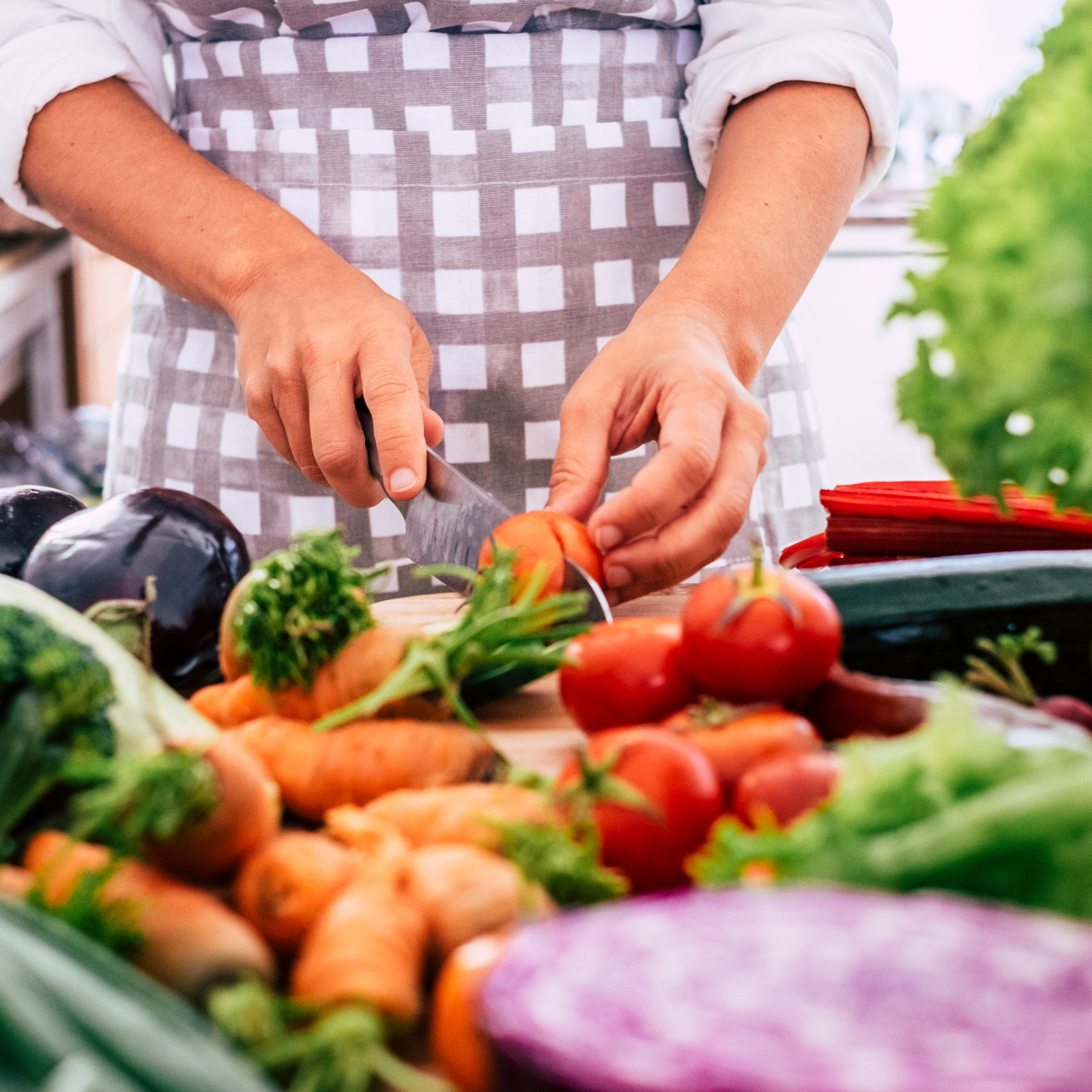 Person chopping tomatoes surrounded by colorful fresh vegetables, illustrating whole food meal prep for family health.
