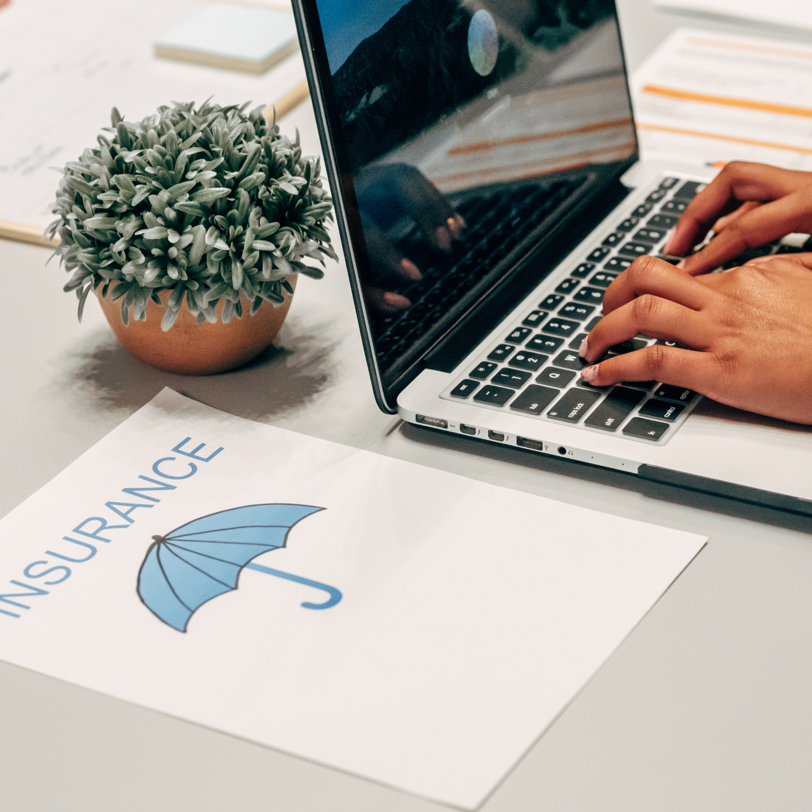 Hands typing on a laptop with an insurance document featuring a blue umbrella icon nearby