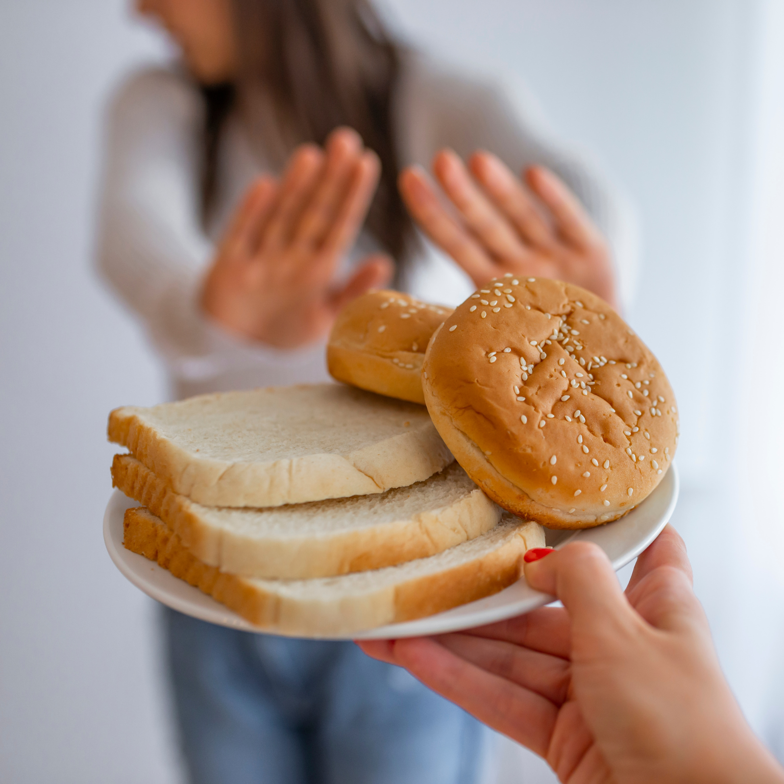 Woman rejecting a plate of white bread and hamburger buns, symbolizing gluten or gut sensitivities.