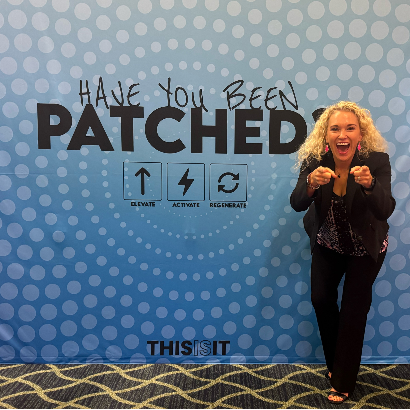 Rachael DeBoy smiling and pointing in front of LifeWave event backdrop promoting the X39 stem cell patch.