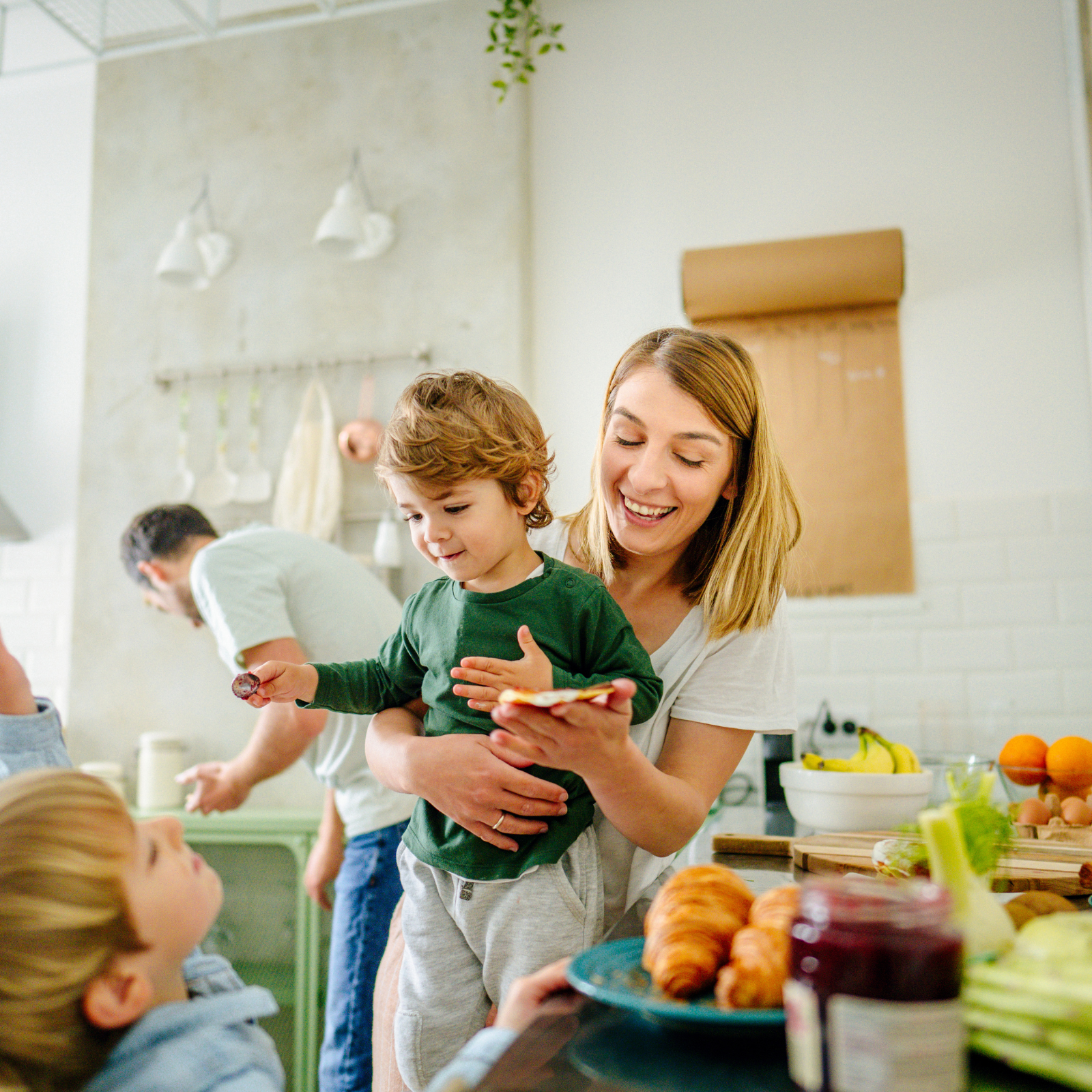 Happy family with young kids preparing breakfast in a cozy kitchen, surrounded by healthy food and croissants.