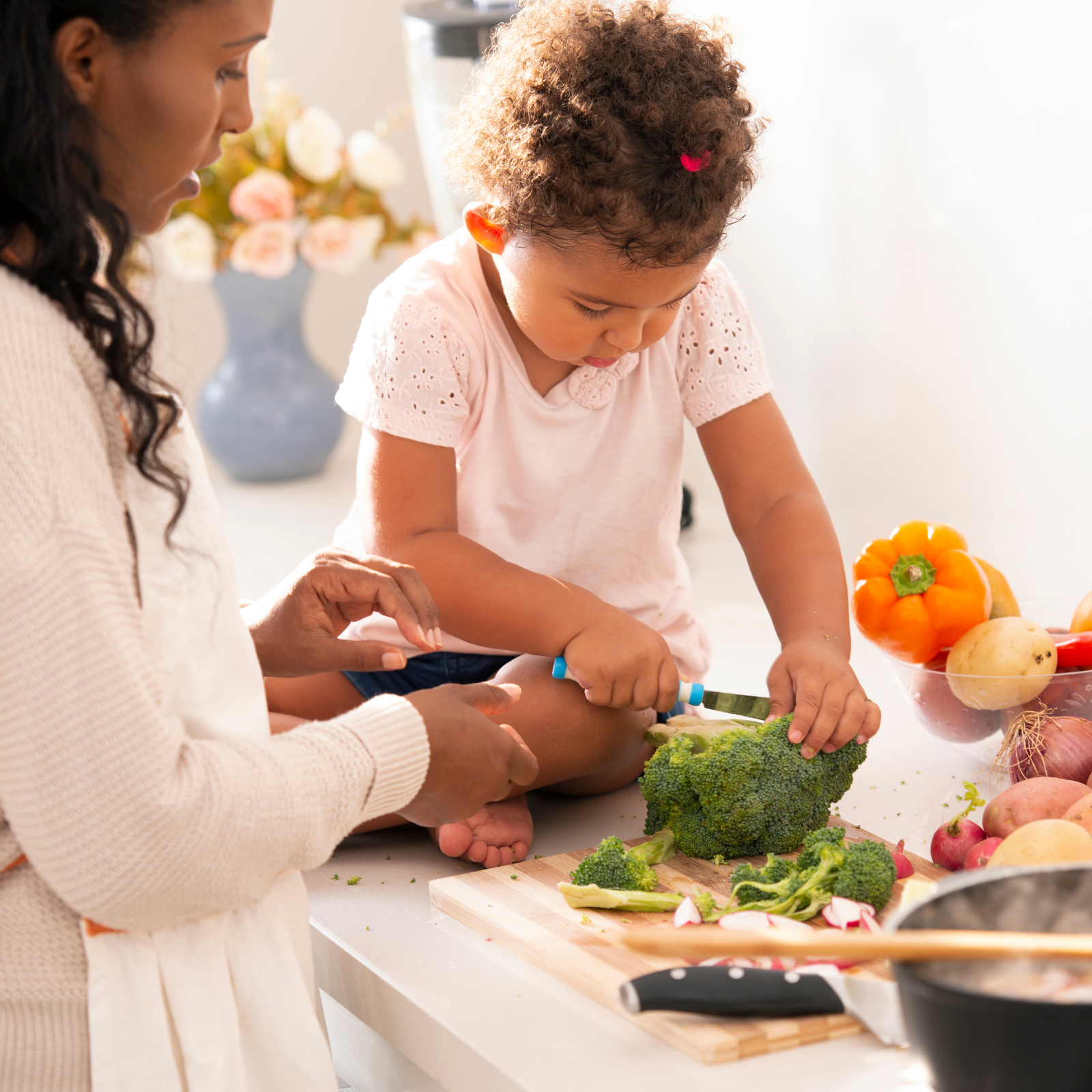 Parent helping child chop broccoli on cutting board during family meal prep