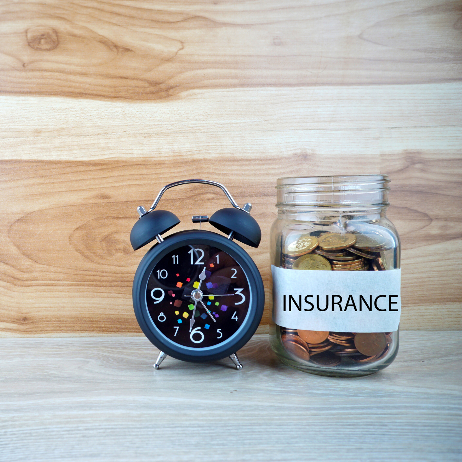 Alarm clock beside jar labeled insurance filled with coins representing wealth planning